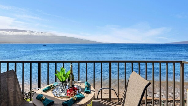 Uma varanda com mesa posta para dois, com vista para um mar calmo e montanhas ao longe.