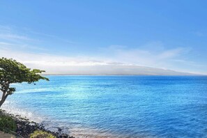 A coastal view with a clear sky, calm sea, and a distant mountain range. - Oceanfront 2 Bedroom Oasis on Sugar Beach (Wailuku)