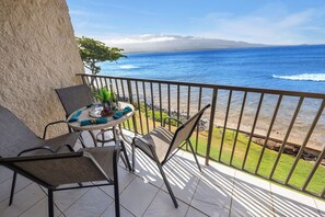 A balcony with a view of the ocean, a table with chairs, and a potted plant. - Oceanfront 2 Bedroom Oasis on Sugar Beach (Wailuku)