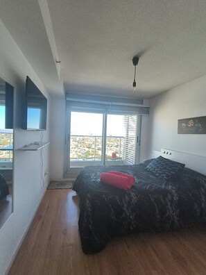 Un dormitorio con una cama, un televisor montado en la pared y una ventana con persianas.