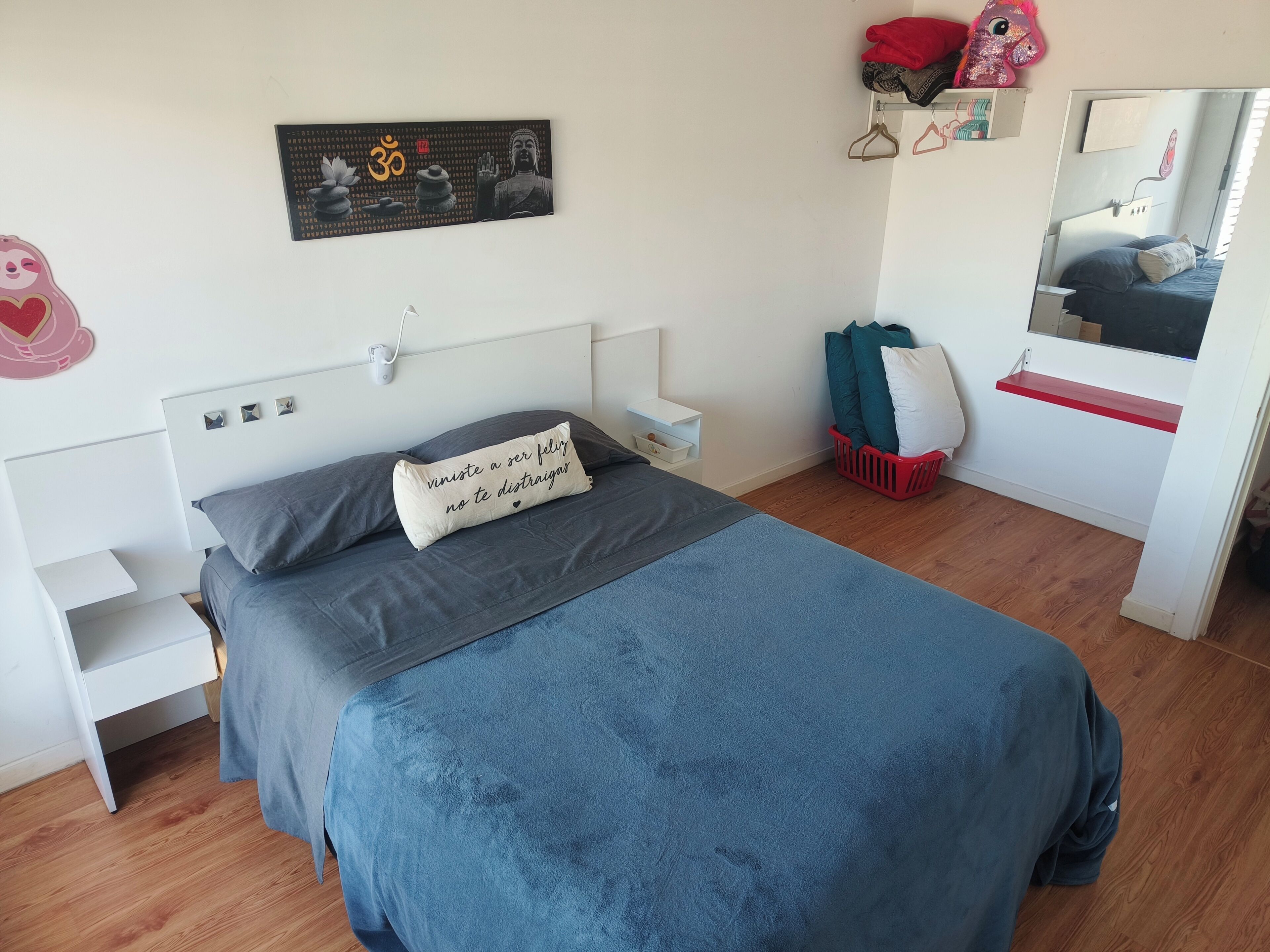 A bedroom with a bed, a nightstand, a wall-mounted shelf, a mirror, and a wall decoration.
