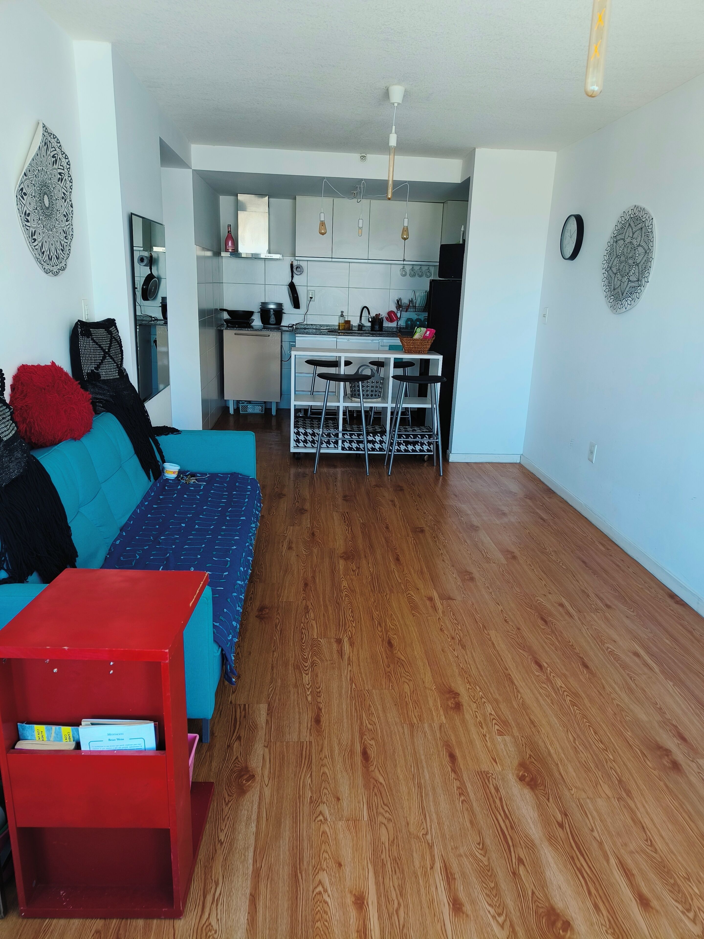 A modern living room with a sofa, a red table, and a kitchen area with a dining table and chairs.