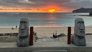 A beach with two stone statues, a sunset, and a calm sea.