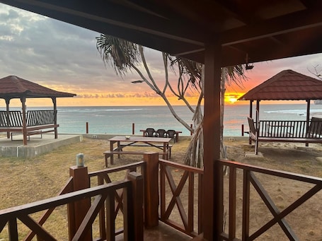 A beachside pavilion with a view of the ocean and a sunset.. Mama Nings Beach Hotel