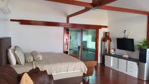 A spacious room with a large bed, a sofa, a dining area, and a kitchen.
