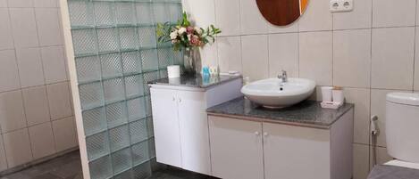 A bathroom with a glass shower enclosure, a white sink, a mirror, and a patterned rug.