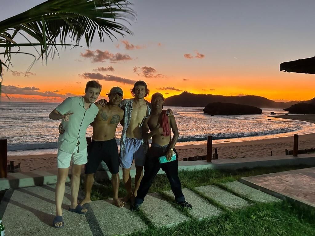 A group of people standing on a concrete path by the beach at sunset.
