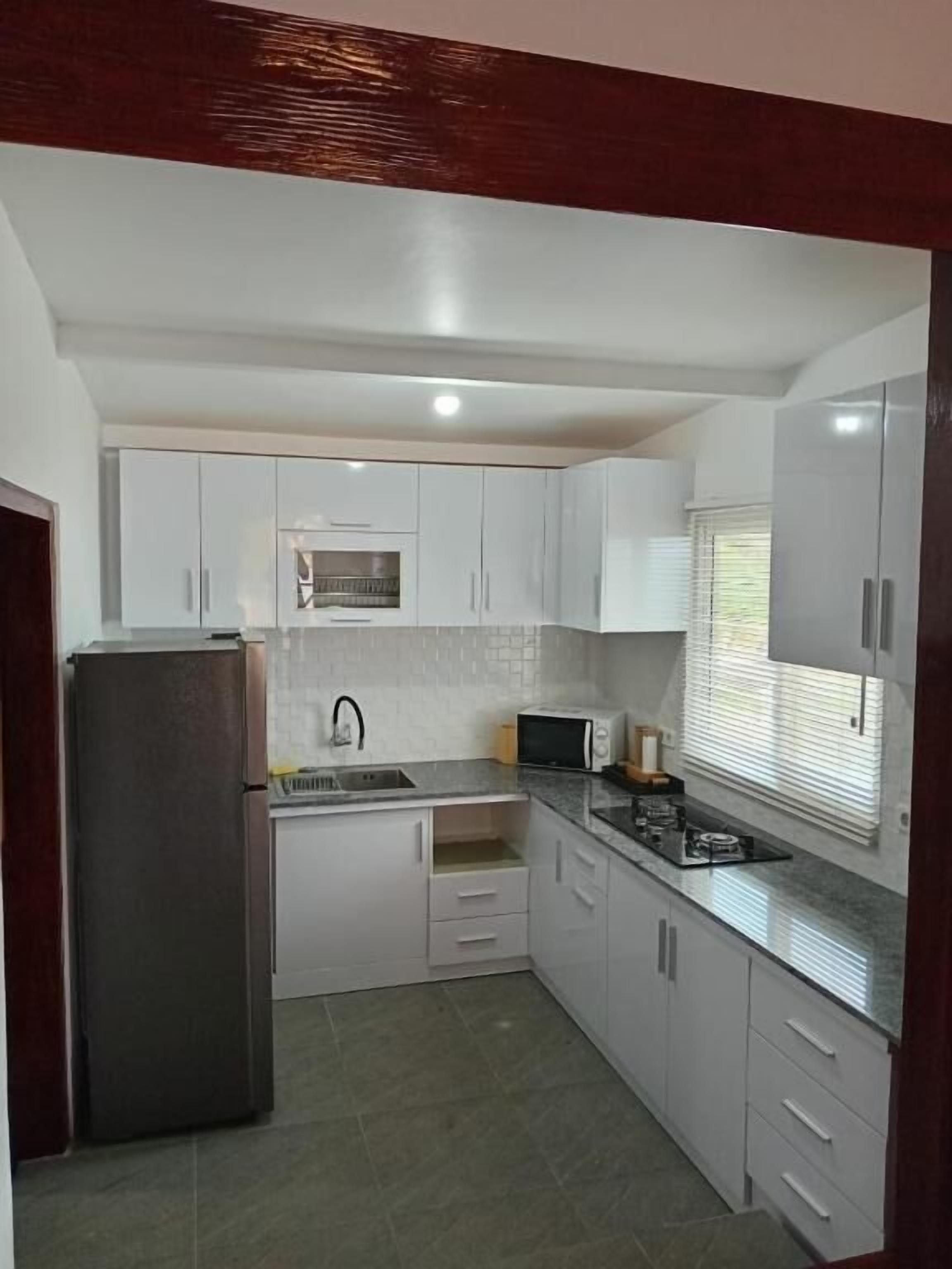 A compact kitchen with white cabinets, a stainless steel refrigerator, a microwave, and a gas stove.