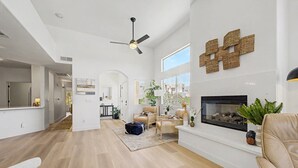 Una sala de estar amplia con chimenea, ventilador de techo y un ventanal grande.