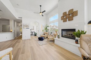 Ein großzügiges Wohnzimmer mit Kamin, Deckenventilator und großem Fenster.