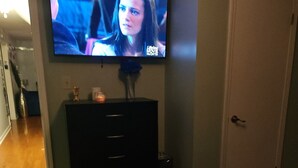 Una camera da letto con un letto, una cassettiera, una televisione appesa al muro e una porta.