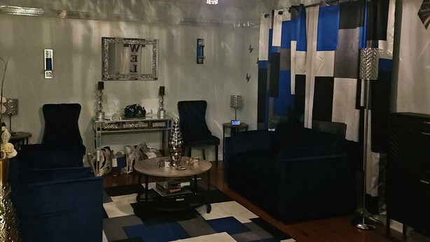 Un soggiorno con un lampadario, divani blu, un tavolino da caffè e un tappeto decorato.