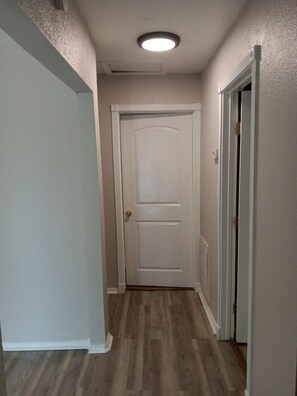 A hallway with a white door, wooden flooring, and a ceiling light. - Tranquil 2-bedroom house with AC in Orange Grove (Orange Grove)
