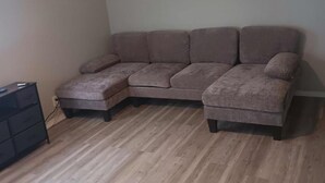 Habitación de esquina con sofá modular, ventilador de techo y piso de madera.