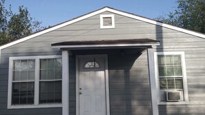 Una casa de un piso con puerta principal, dos ventanas y un porche pequeño.