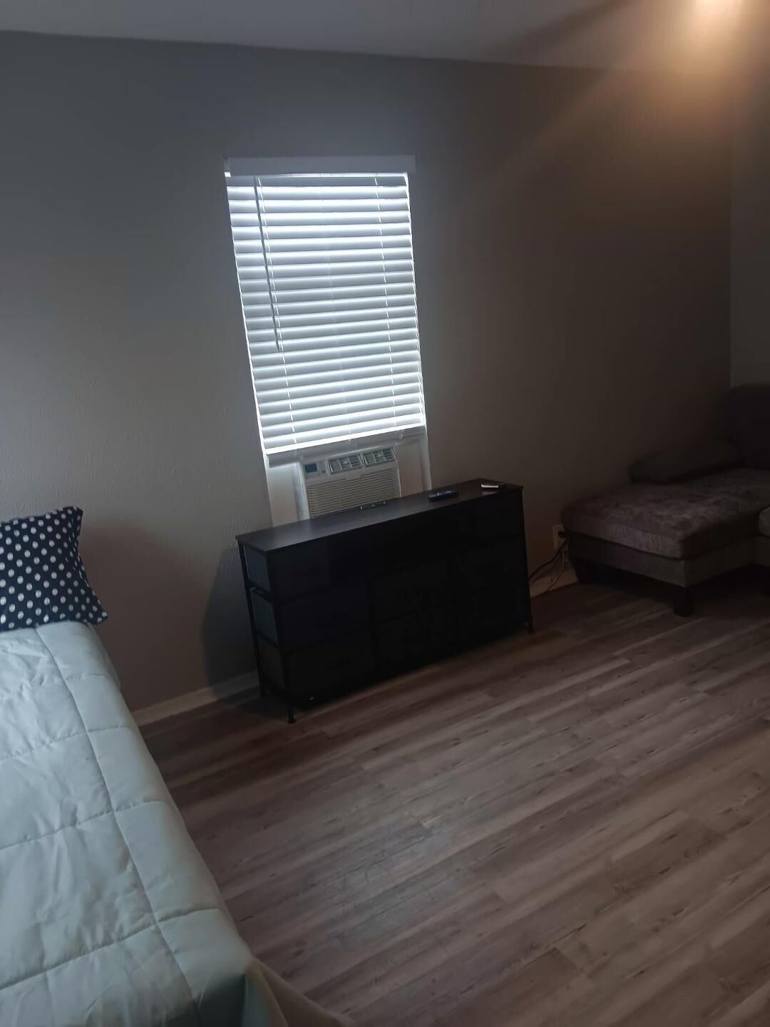 Una habitación con una cama, un mueble negro pequeño, una ventana con persianas y un sofá.