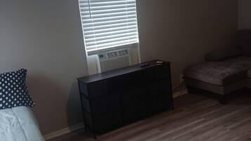 Una habitación con una cama, un mueble negro pequeño, una ventana con persianas y un sofá.
