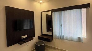 Habitación con una televisión montada en la pared, un espejo grande, una ventana con cortinas y un cesto de basura.