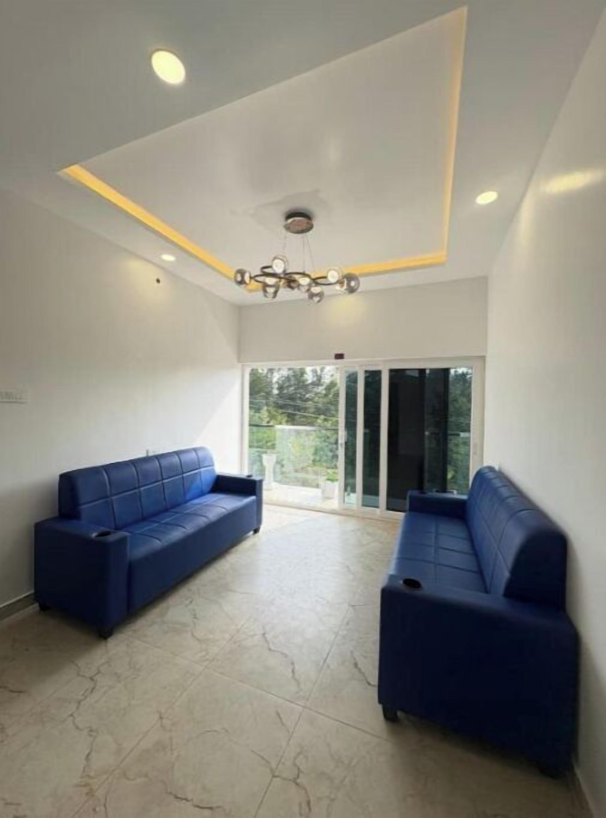 A room with two blue sofas, a ceiling light fixture, and a view through a glass door.