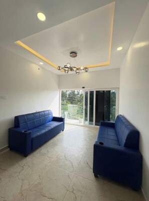 A room with two blue sofas, a ceiling light fixture, and a view through a glass door. - RATHNA RESIDENCY YERCAUD (Yercaud)