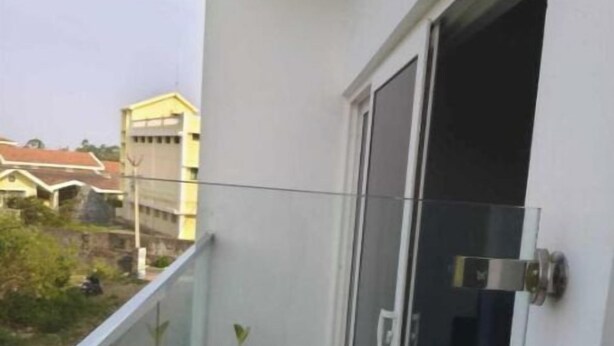 Un balcón con puerta de cristal, plantas en macetas y vista a edificios al fondo.