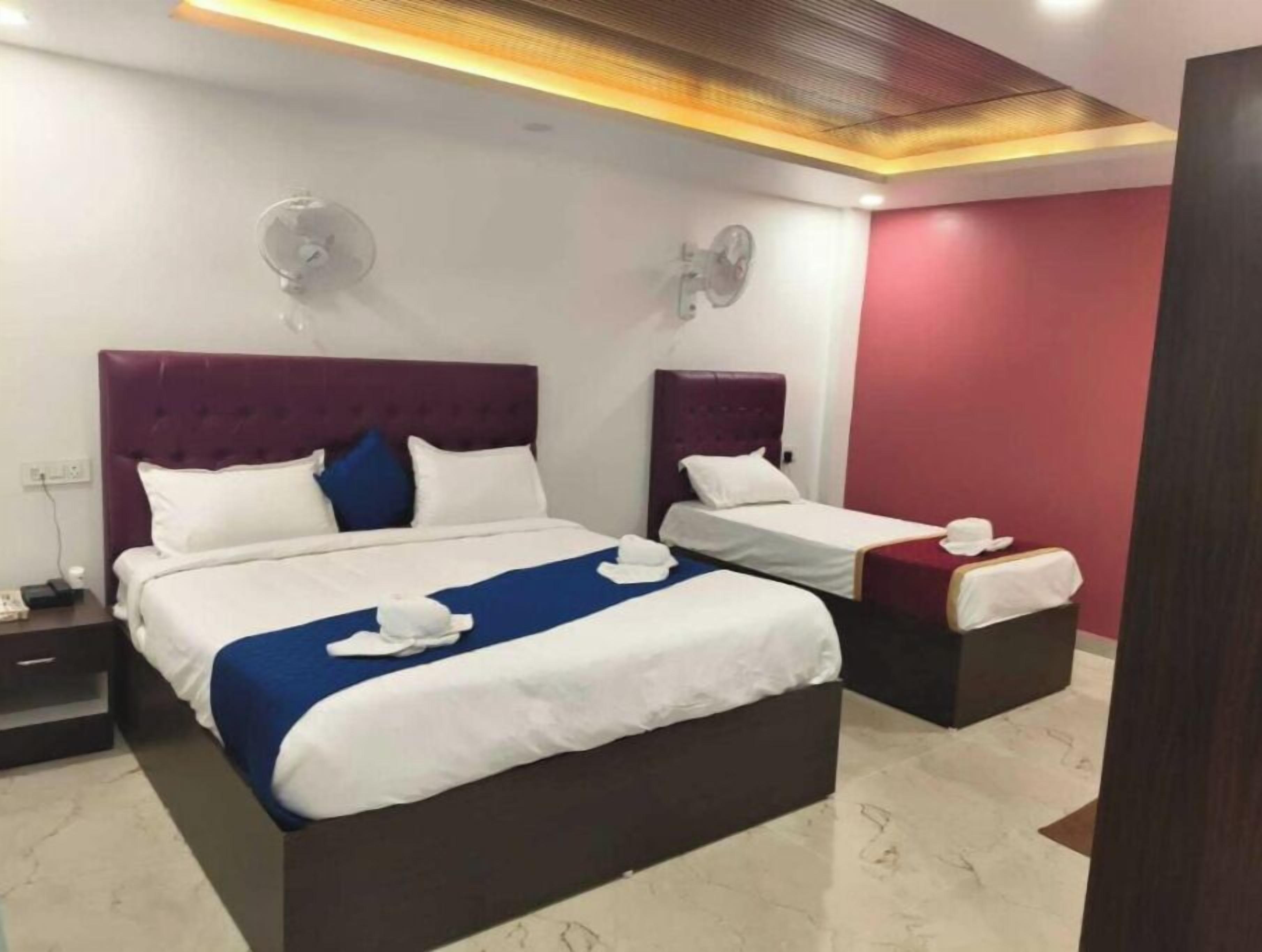 A hotel room with two beds, a nightstand, a wall clock, and a ceiling fan.
