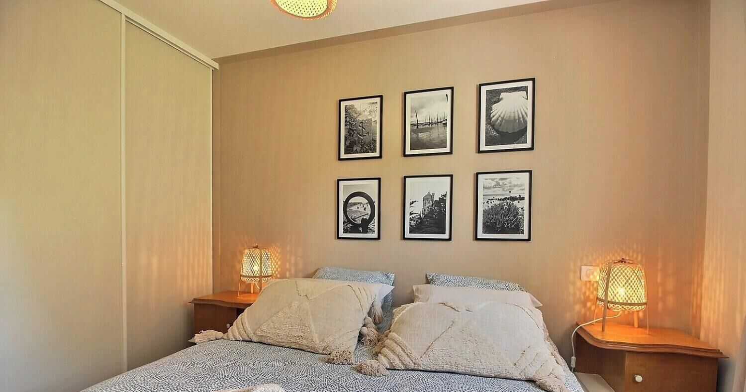 Un dormitorio con una cama, dos lámparas de noche y seis cuadros en la pared.