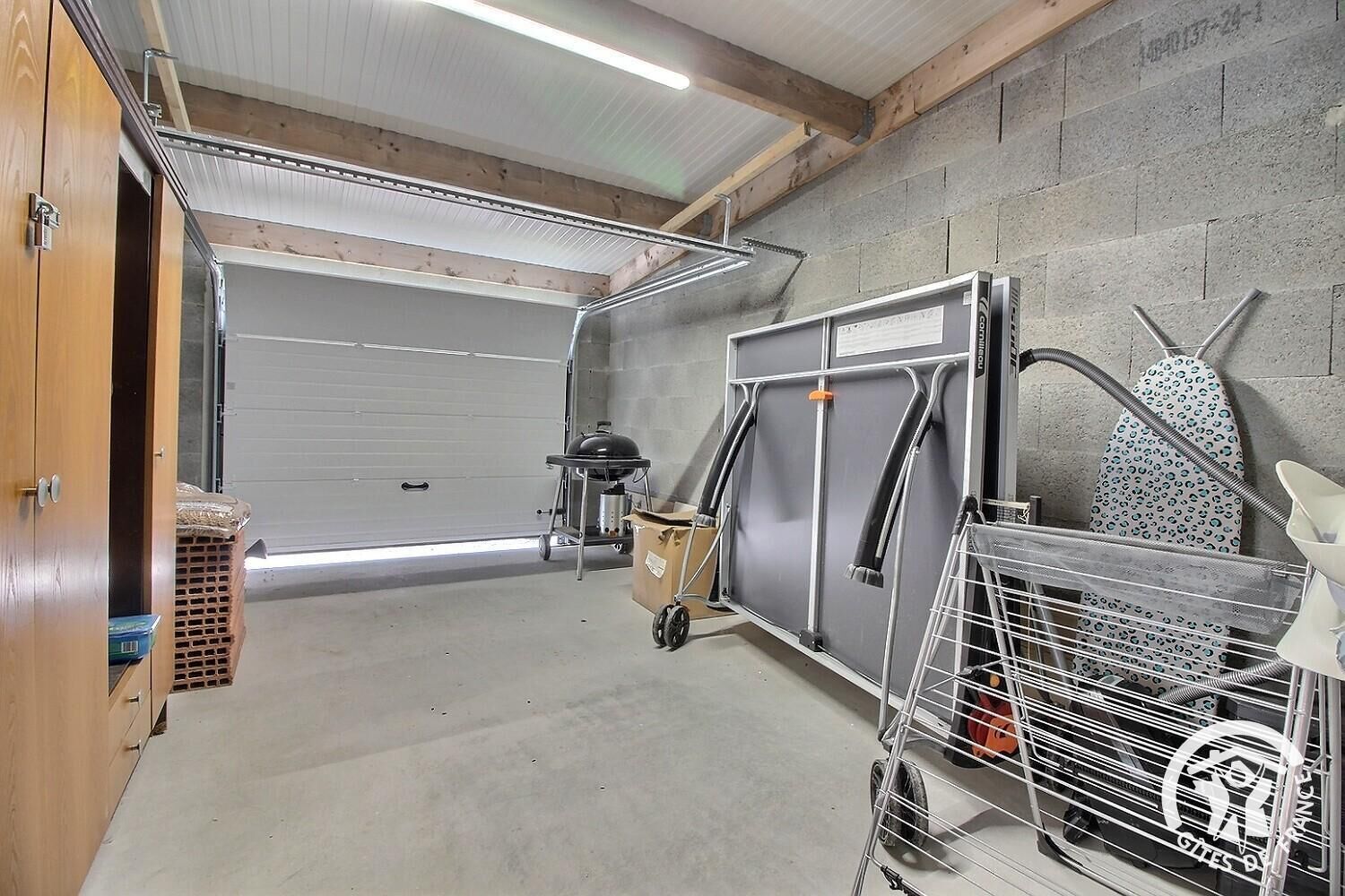 A garage with a concrete floor, a closed garage door, and a metal cart with a grill.