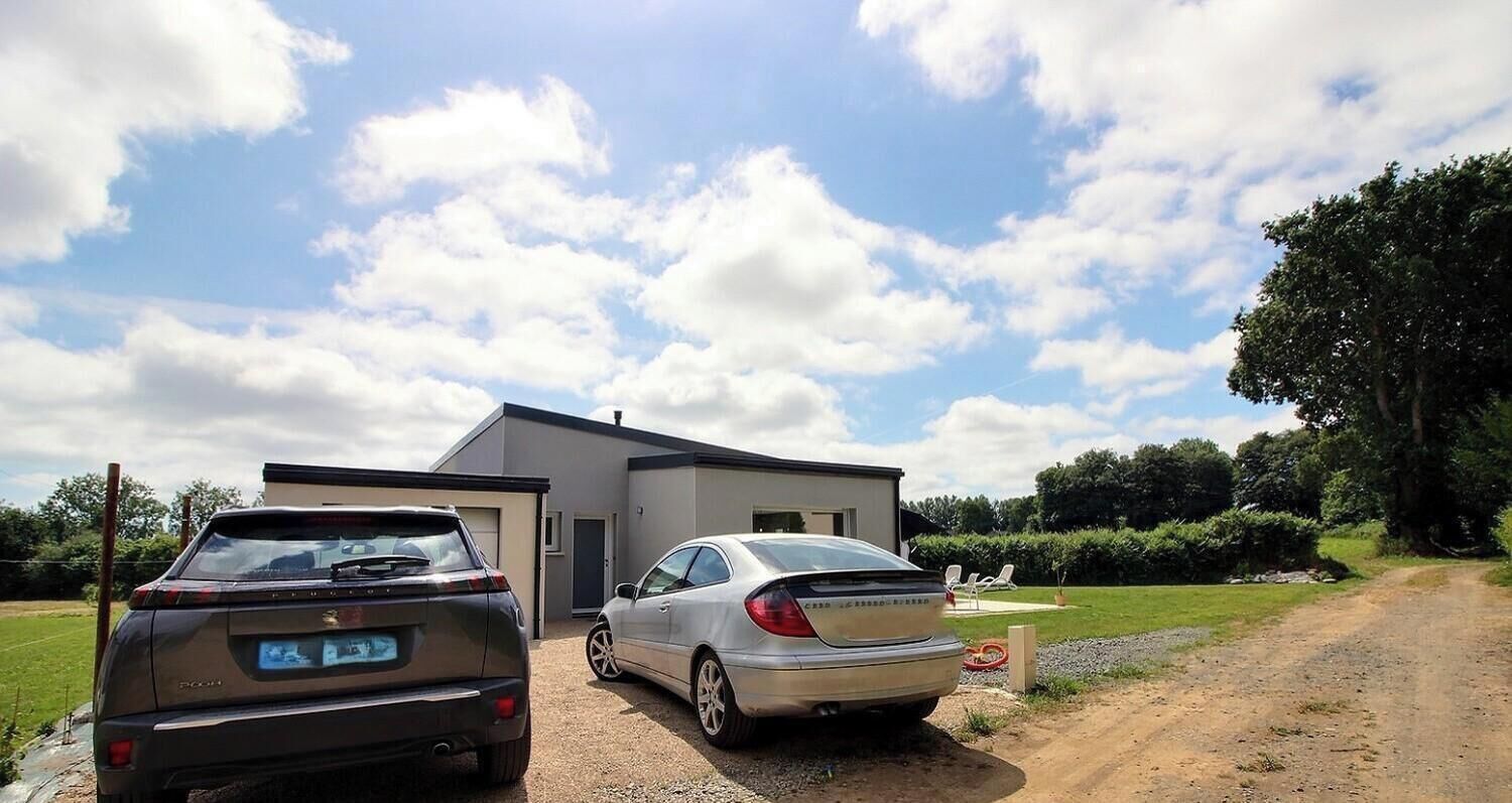 Dois carros estacionados em frente a um edifício moderno com acesso por caminho de cascalho.