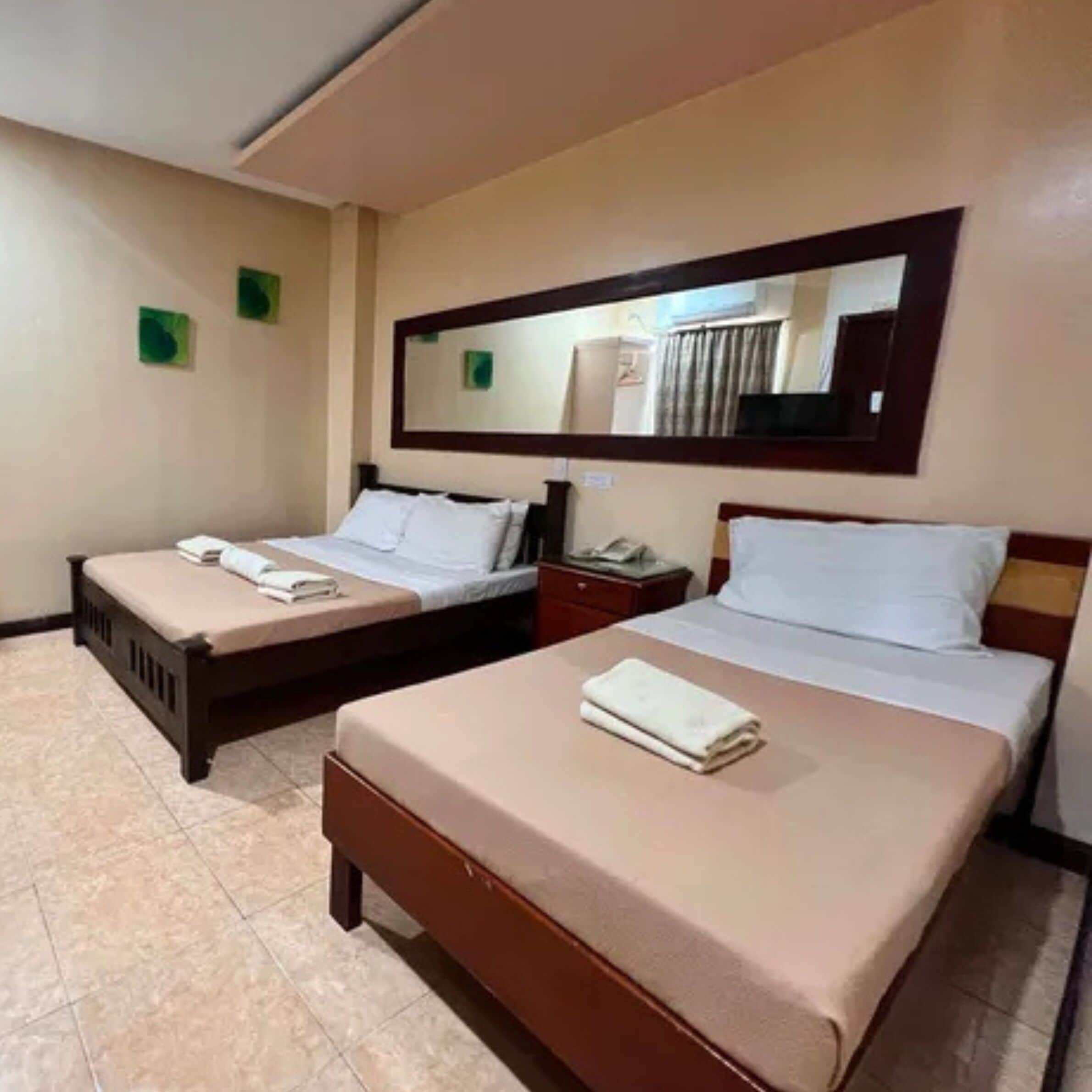 A hotel room with two beds, a large mirror, and a small bedside table with a lamp.