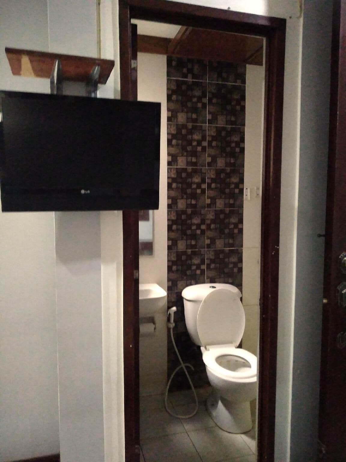 A bathroom with a toilet, sink, and a mounted television.