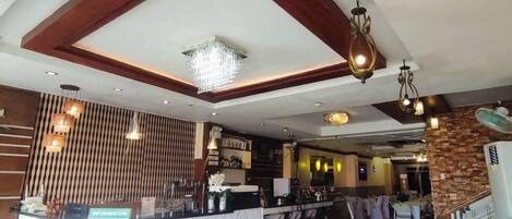 Un restaurante con zona de bar, vigas de madera en el techo y una araña.