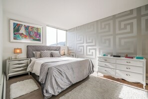A bedroom with a bed, nightstands, a dresser, a rug, and a wall with a geometric pattern.