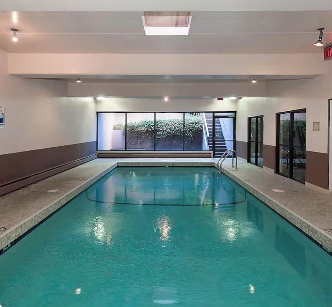 An indoor swimming pool with clear glass walls, a visible exit sign, and a staircase leading outside.