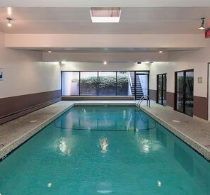 An indoor swimming pool with clear glass walls, a visible exit sign, and a staircase leading outside.
