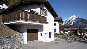 A two-story building with a wooden balcony, a garage, and a mountain view. - 2001 Haus Alvaneu by Interhome (Alvaneu Dorf)