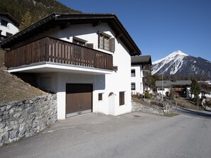 Ein zweistöckiges Gebäude mit einem Holzbalkon, einer Garage und Blick auf die Berge.