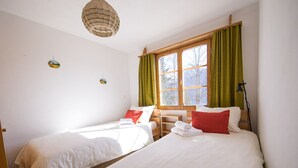 A room with two beds, a window with curtains, a hanging light fixture, and wall decorations. - 2001 Haus Alvaneu by Interhome (Alvaneu Dorf)