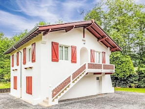 Ein weißes Gebäude mit roten Fensterläden, einem Balkon und einer Treppe, die zum Eingang führt.