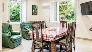 Comedor con mantel a cuadros, sillas de cuero verde y vistas a follaje a través de ventanas abiertas.