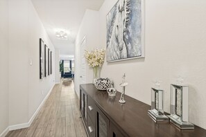 Ein Flur mit einer dunklen Holztruhe, einer weißen Vase mit Blumen und einem großen abstrakten Gemälde eines Pferdes.