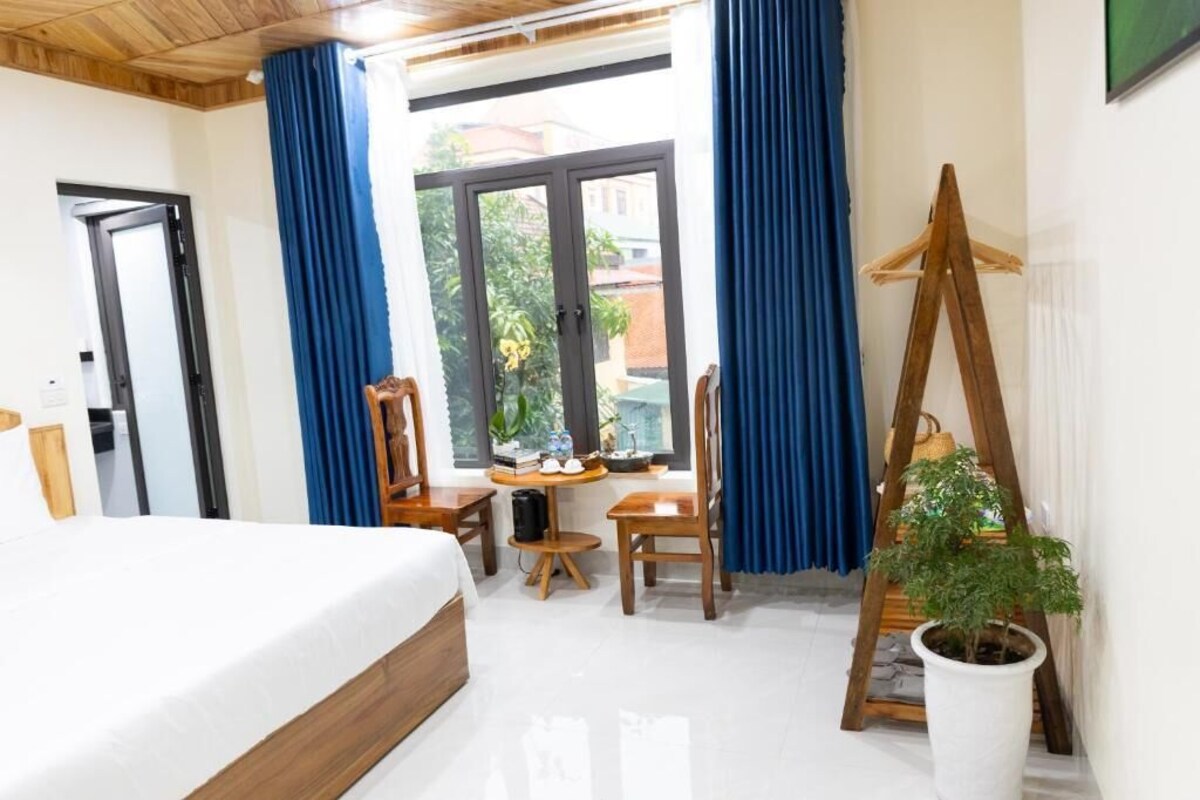 A hotel room with a bed, a desk, a chair, a potted plant, and a wooden easel.