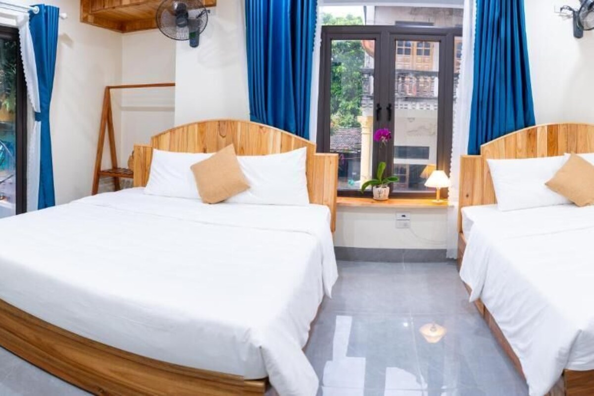 A room with two wooden beds, a small table with a lamp, and a window with curtains.