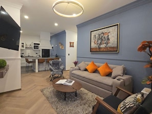 A modern living room with a grey sofa, orange cushions, a coffee table, and a painting on the wall. - Departamento Raziel 118 (Val'Quirico)