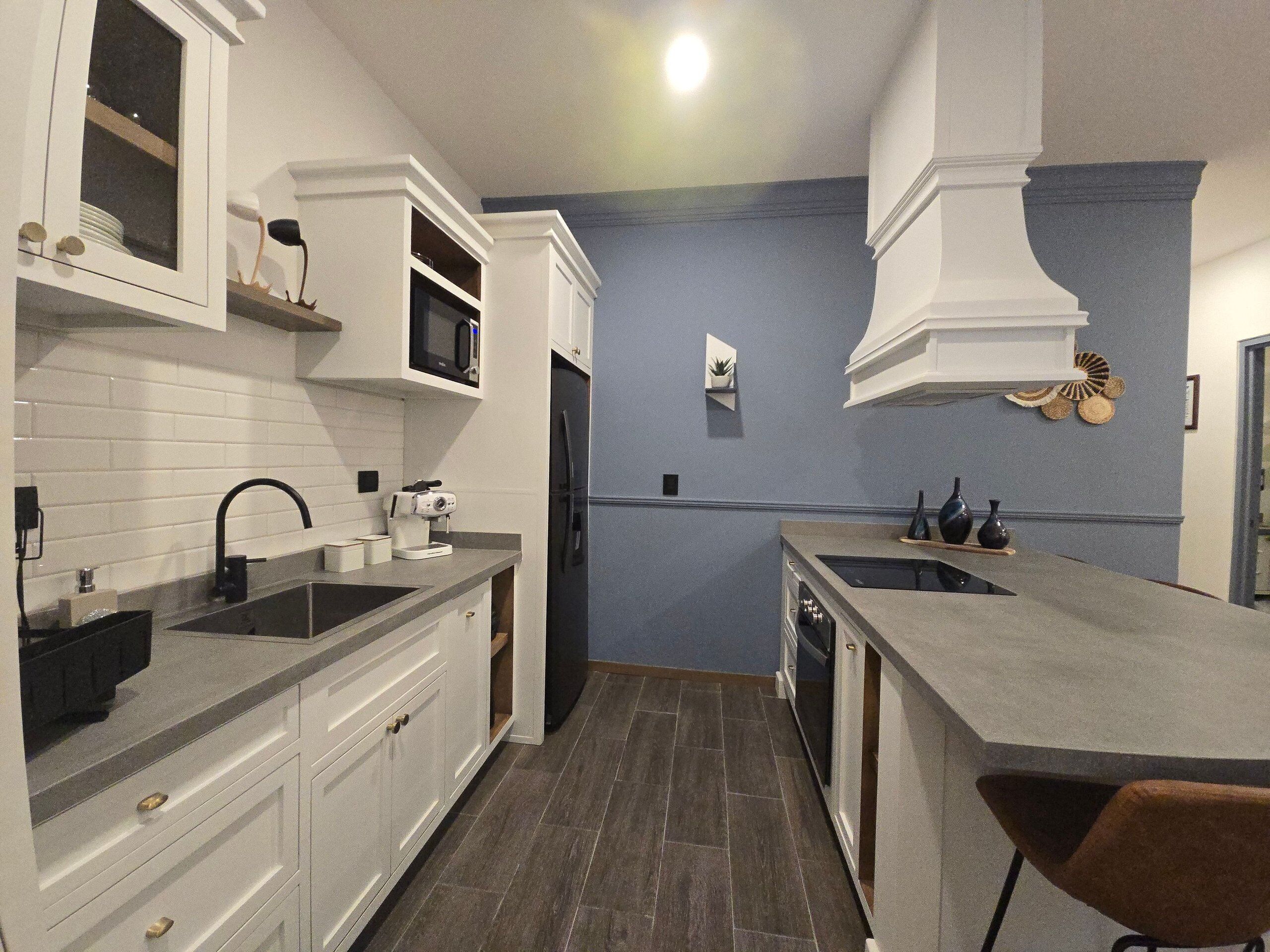Una cucina compatta con mobili bianchi, un forno a microonde integrato e un lavello in acciaio inossidabile.