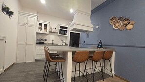 A modern kitchen with white cabinetry, a central island with bar stools, a microwave, and a blue accent wall. - Departamento Raziel 118 (Val'Quirico)