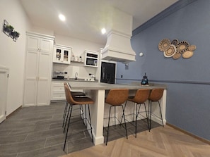 A modern kitchen with white cabinetry, a central island with bar stools, a microwave, and a blue accent wall. - Departamento Raziel 118 (Val'Quirico)