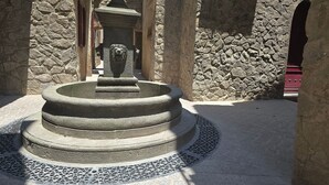A stone fountain with a lion head, surrounded by stone walls and a tiled floor. - Departamento Raziel 118 (Val'Quirico)