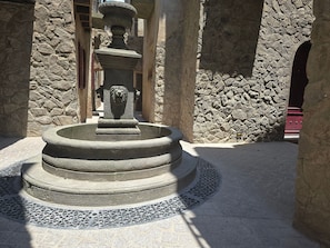 A stone fountain with a lion head, surrounded by stone walls and a tiled floor. - Departamento Raziel 118 (Val'Quirico)