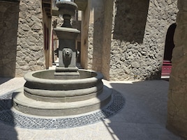 Una fuente de piedra con cabeza de león, rodeada de muros de piedra y un suelo de baldosas.